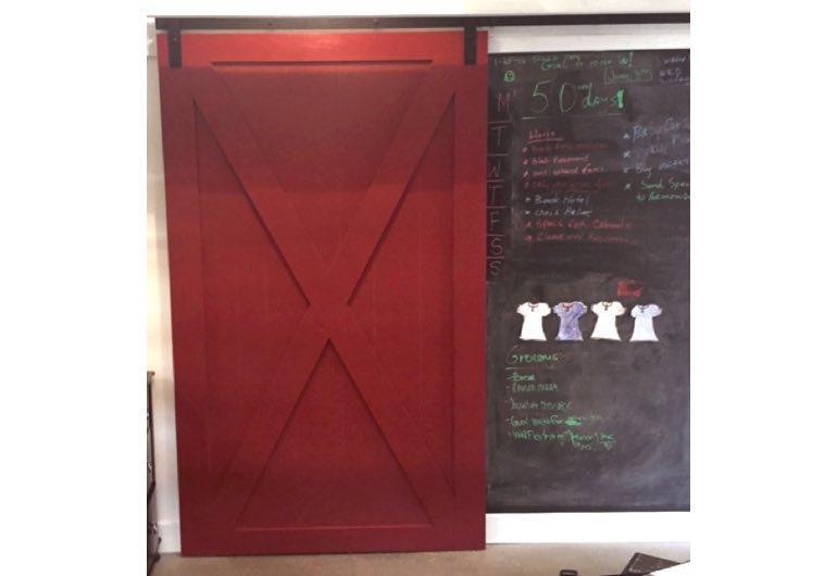 Red sliding barn door with black hardware next to chalkboard 